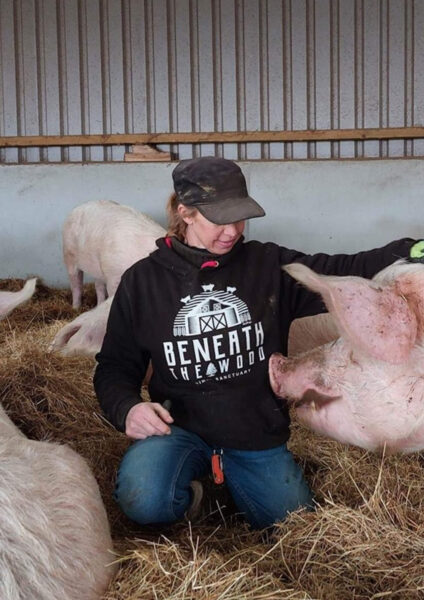 Sasha sat stroking a pig wearing a black hoodie with white print & hot pink trims. By Viva La Vegan. Fund raising for Beneath The Wood Sanctuary
