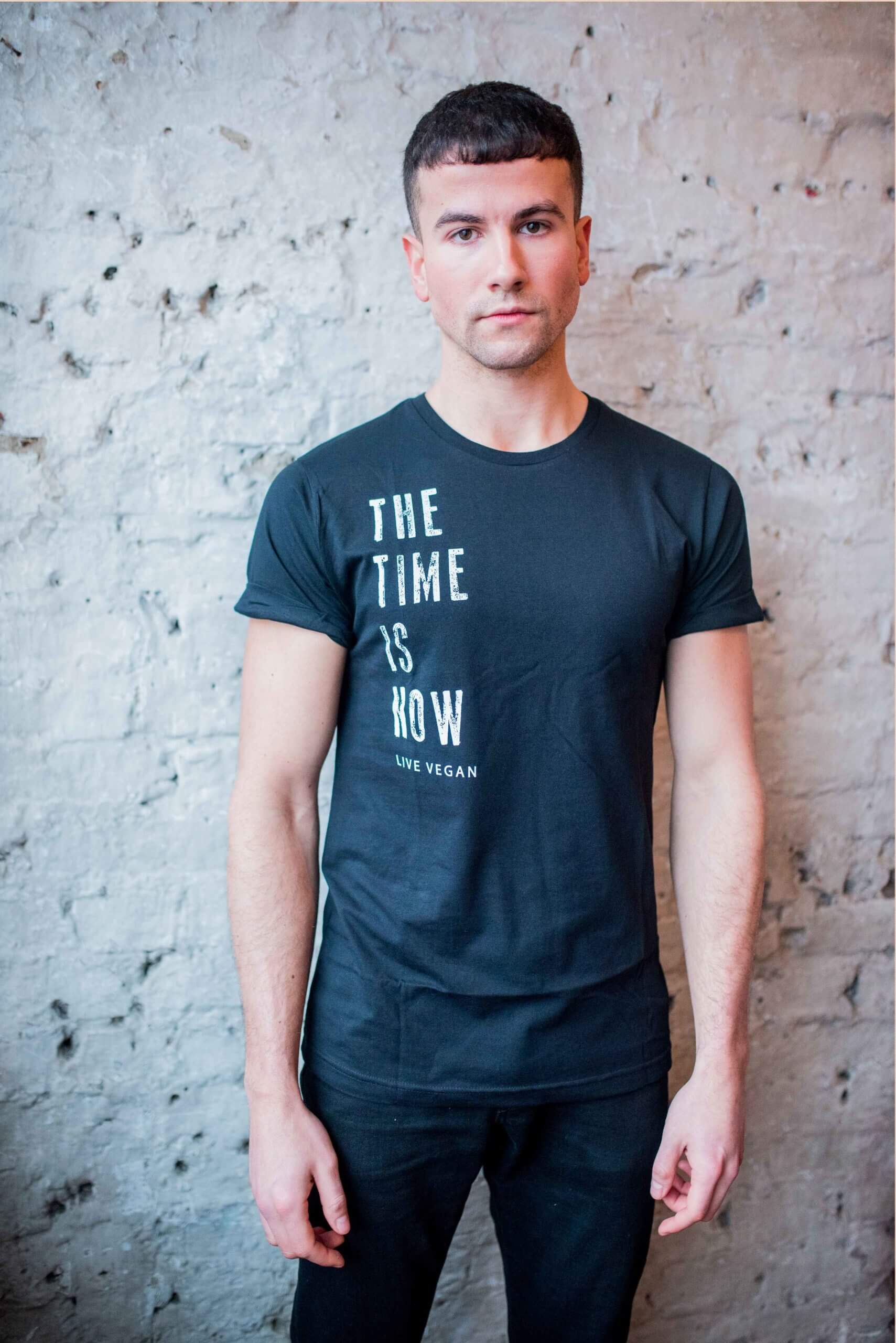 A short haired male model standing in front of wall wearing Viva La Vegan's Time is Now Statement T-shirt.