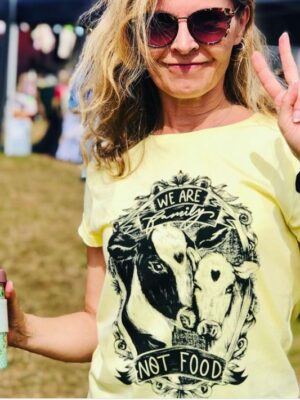 A blonde haired women wearing one of Viva La Vegan lemon coloured vegan t-shirt with an illustration of Coaw and Calf with the statement "Family Not Food"