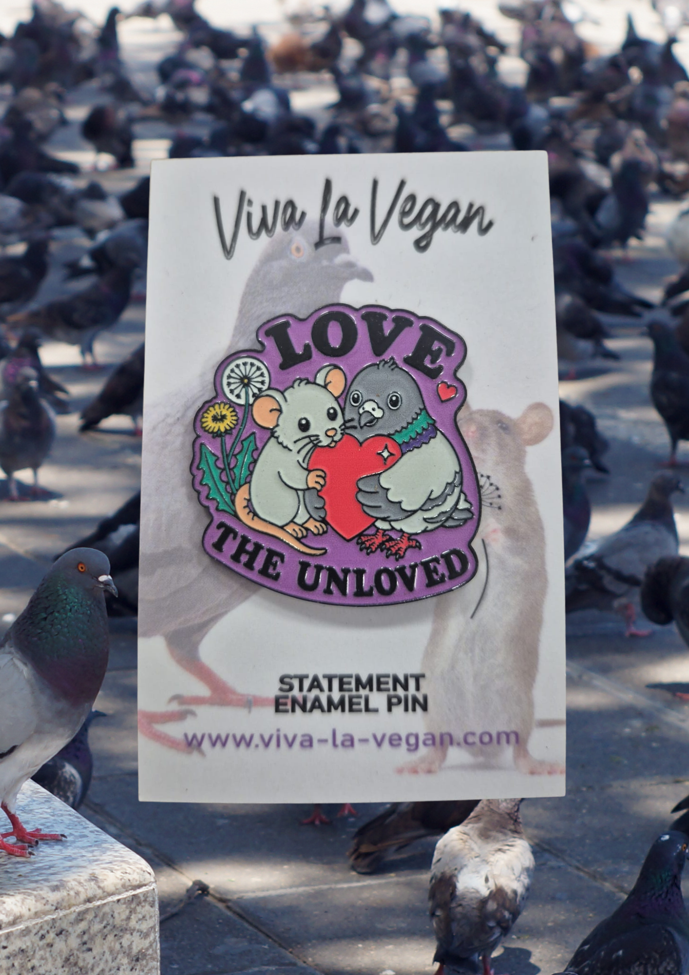 39mm hard enamel pin featuring a rat and pigeon embracing a red heart, surrounded by purple “LOVE THE UNLOVED” lettering and small dandelion details. on a card backer