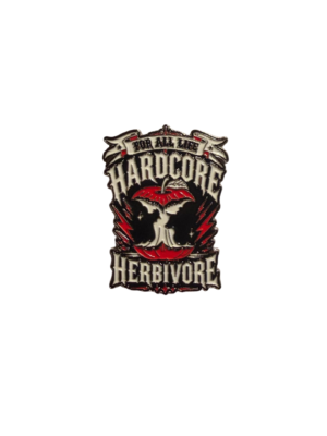 A 38mm hard‑enamel pin featuring a bold red apple with bite marks forming the silhouettes of a cow’s head on one side and a chicken’s head on the other. The apple sits within an edgy “HardCORE Herbivore – For All Life” design, with double clasp/posts on the back for secure wear.
