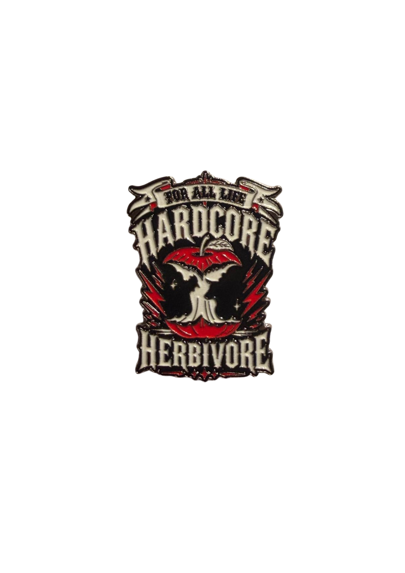 A 38mm hard‑enamel pin featuring a bold red apple with bite marks forming the silhouettes of a cow’s head on one side and a chicken’s head on the other. The apple sits within an edgy “HardCORE Herbivore – For All Life” design, with double clasp/posts on the back for secure wear.